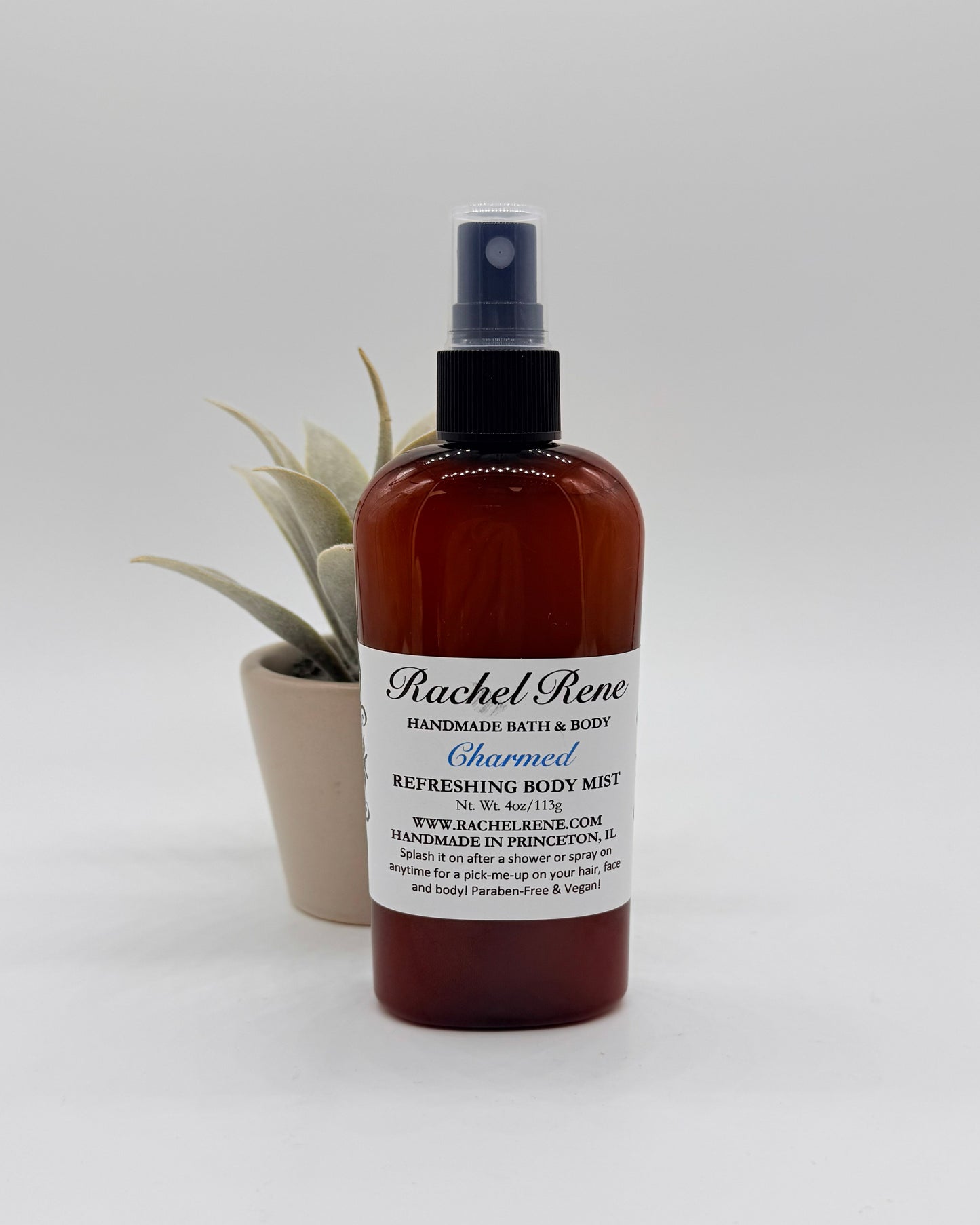 A brown bottle of Charmed Body Mist with black sprayer and white label on a gray background.