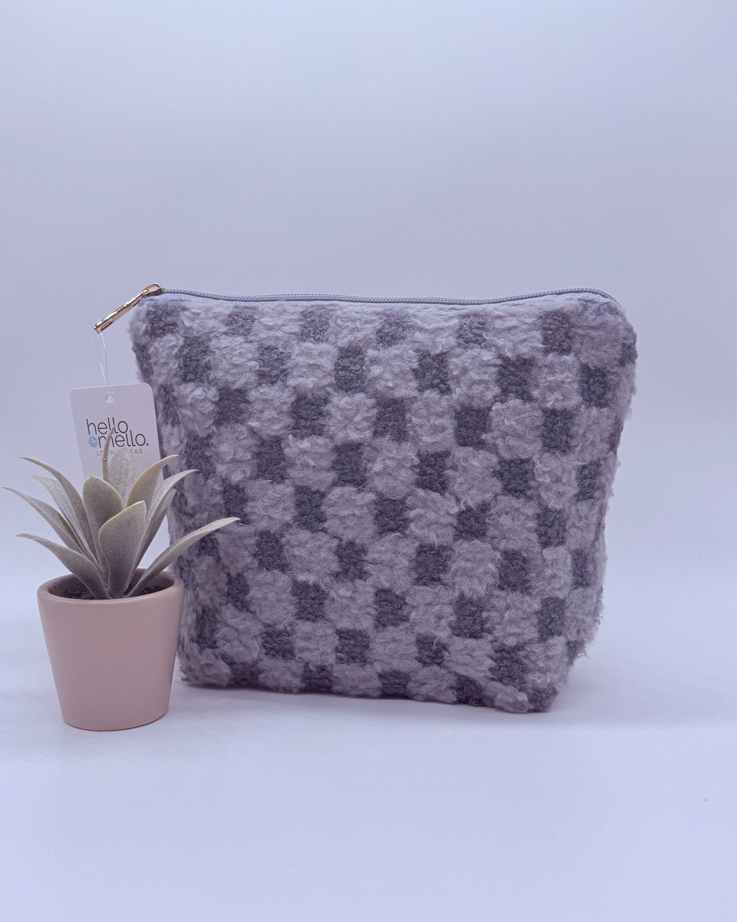 Gray checkered fuzzy cosmetic back with gold zipper top with a plant on a white background
