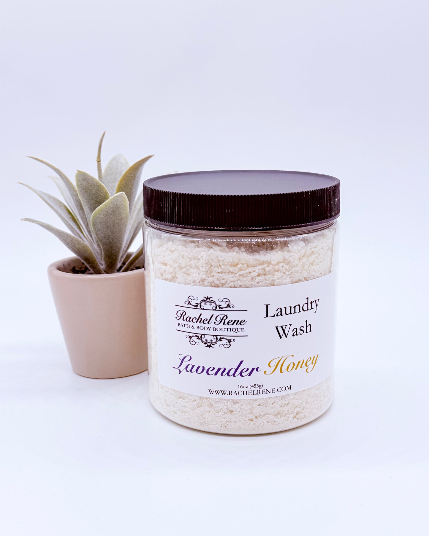 Jar of laundry wash labeled 'Lavender Honey' by Rachel Rene with a plant in the background.