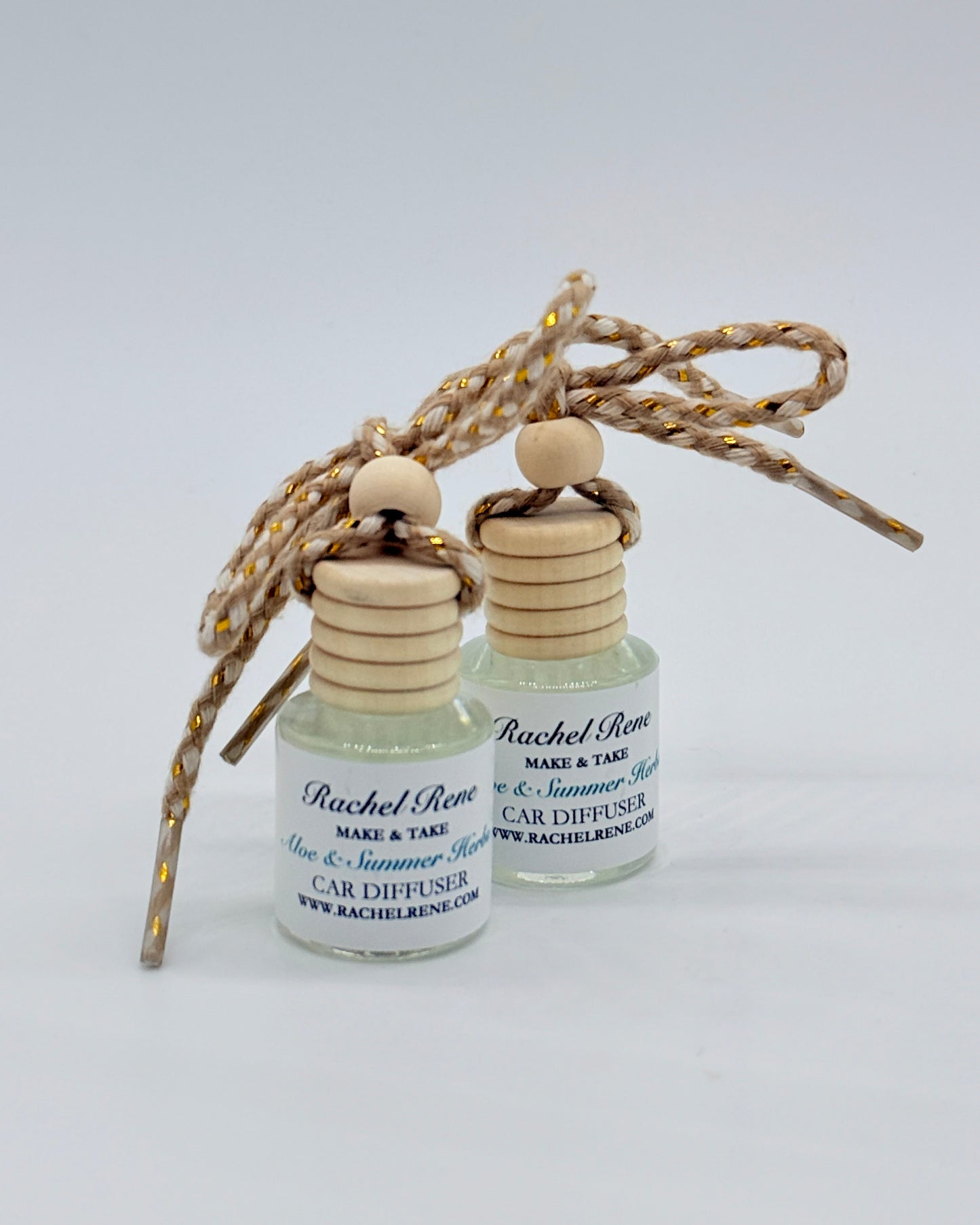 Two bottles of Rachel Rene car diffuser with wooden caps and braided string on a white background