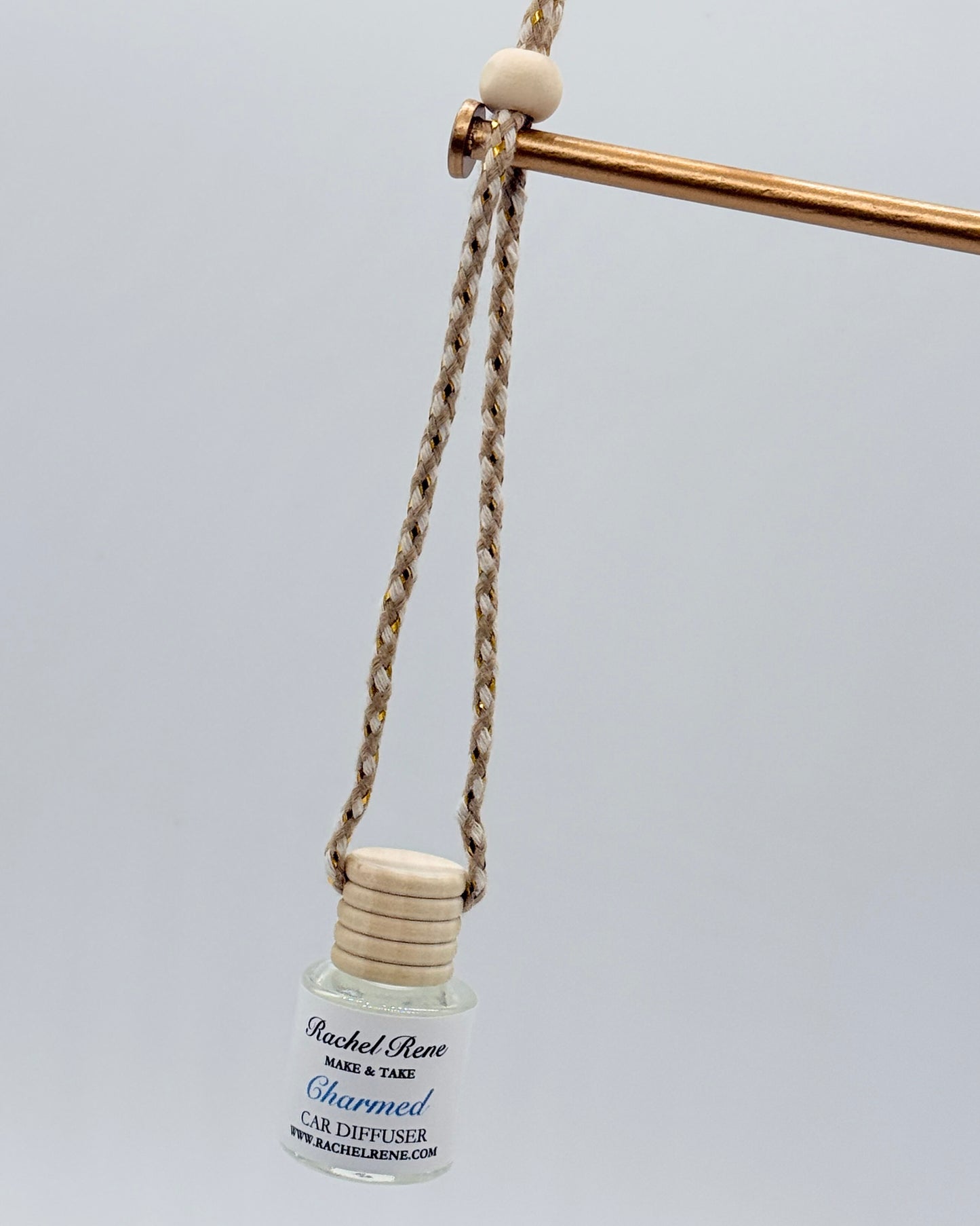 Car diffuser bottle with wooden top on a braided string against a light gray background