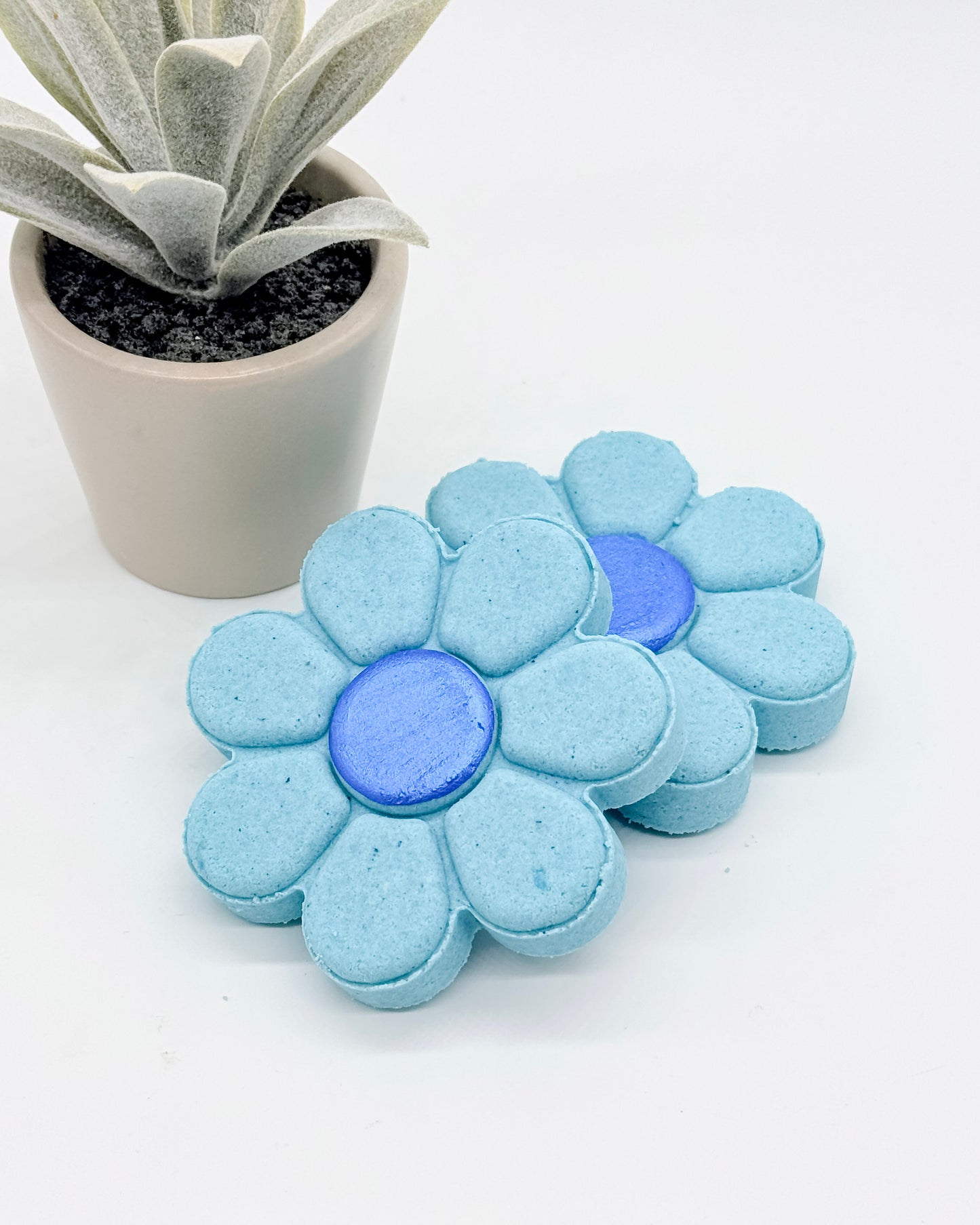 Blue flower-shaped shower bombs with dark blue centers with a potted plant on a white background