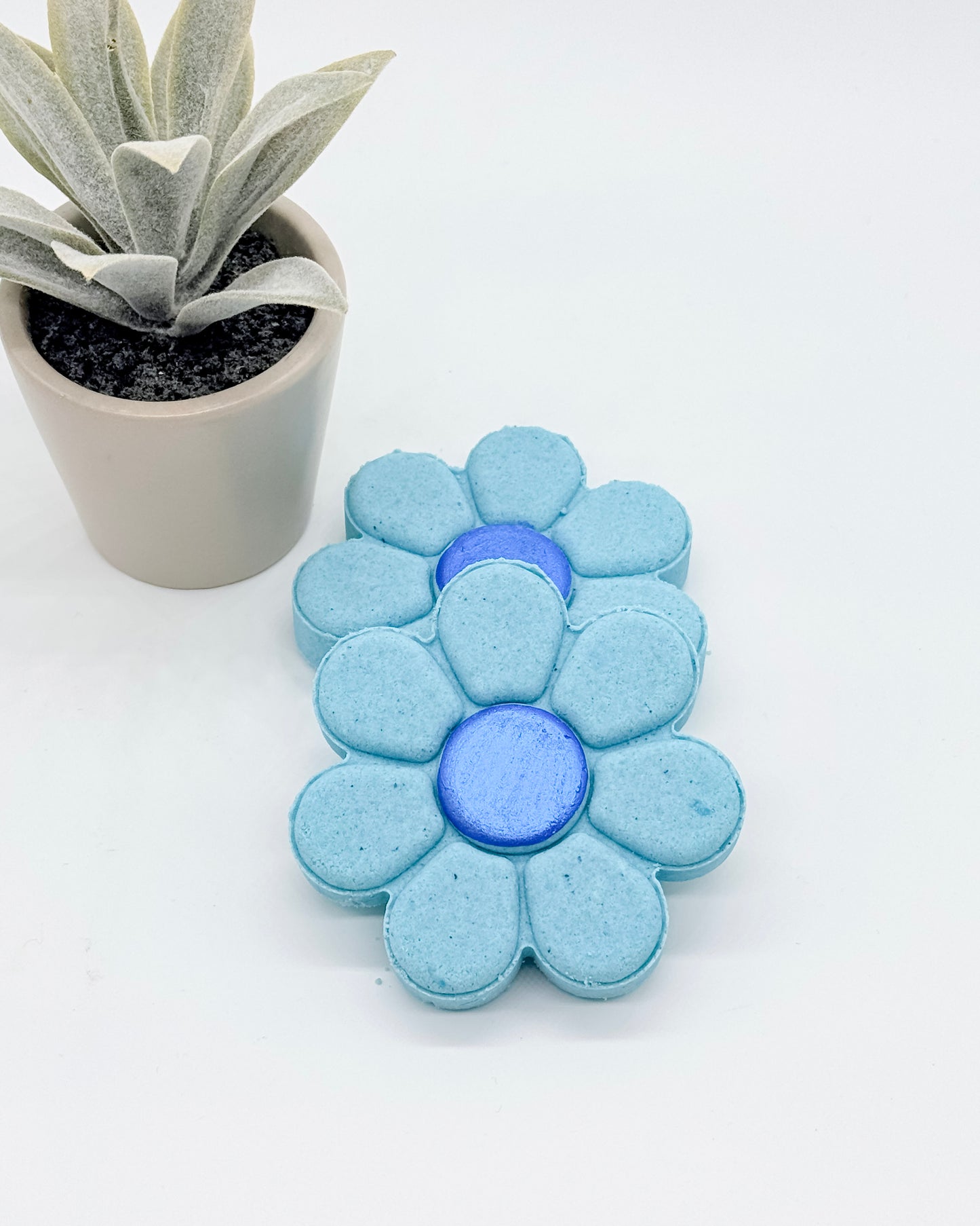 Blue flower-shaped shower bombs with dark blue centers with a potted plant on a white background