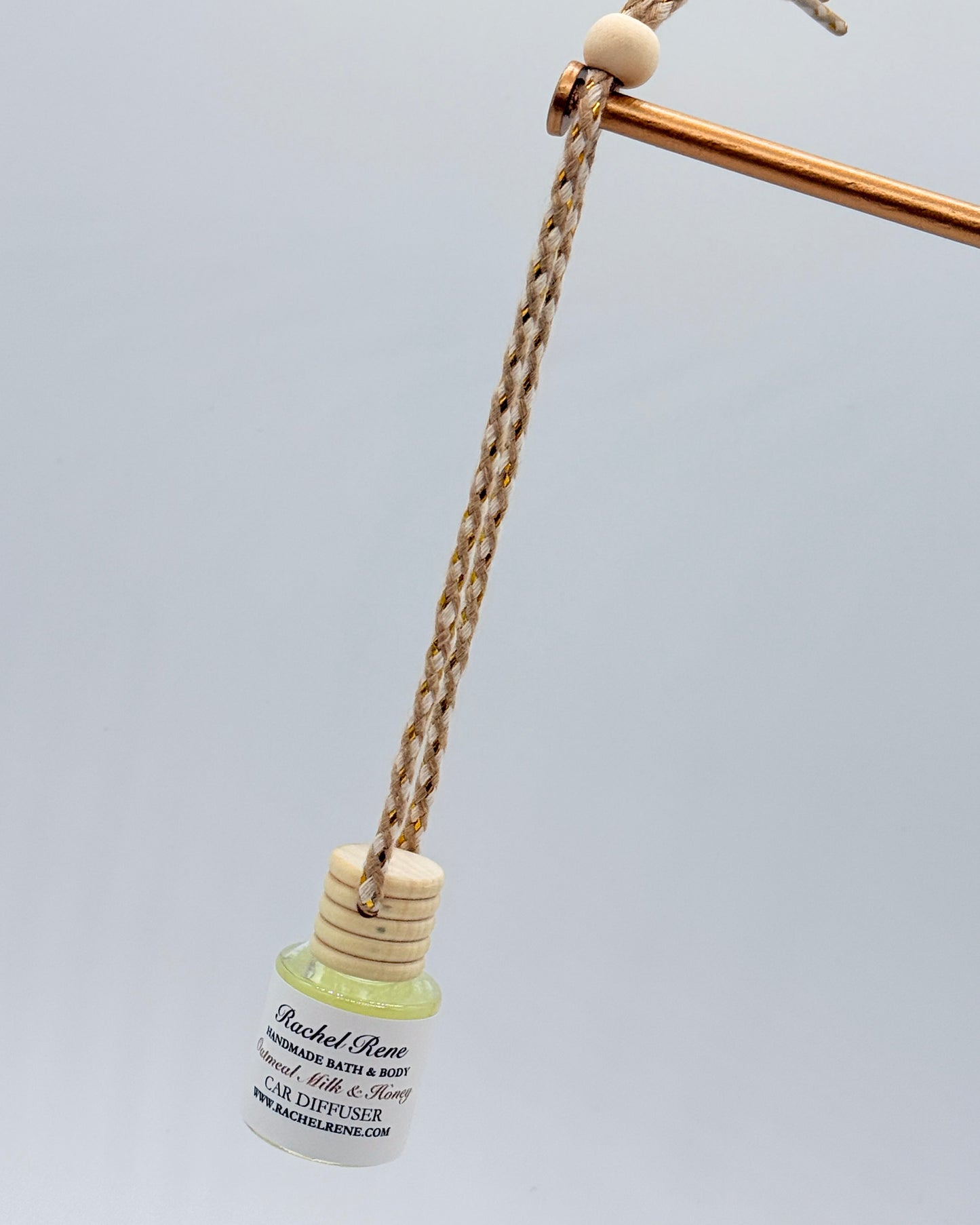 Car diffuser with a wooden top hanging from a braided rope string on a light gray background
