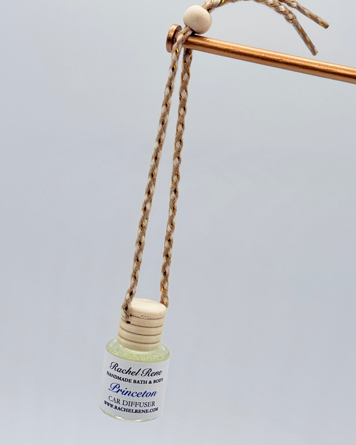 Car diffuser with a wooden top hanging from a braided rope string on a light gray background