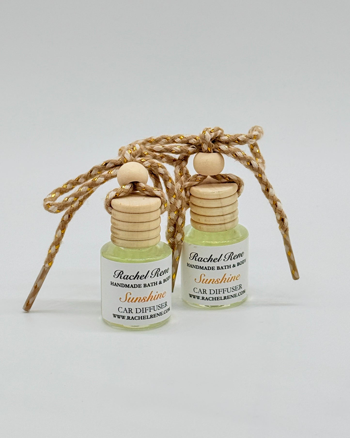 Two bottles of Rachel Rene Car Diffuser with wooden tops and braided string on a white background