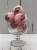 Strawberry scented pink bath bombs that are round and painted with a red strawberry on the top with a green stem