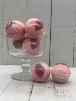 Strawberry scented pink bath bombs that are round and painted with a red strawberry on the top with a green stem