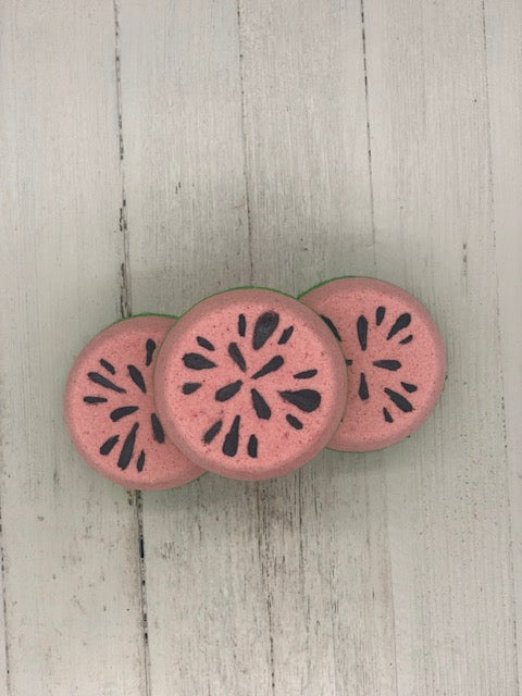 Watermelon scented bubble bombs with green on the bottom and pinkish red on the top half painted with black seeds on the very top