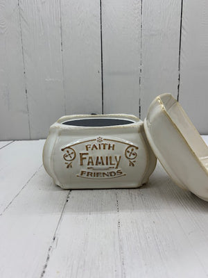 A ceramic wax warmer with the words "Faith, Family, Friends" written in gold on one side. The top cup is detached and leaning on the side.