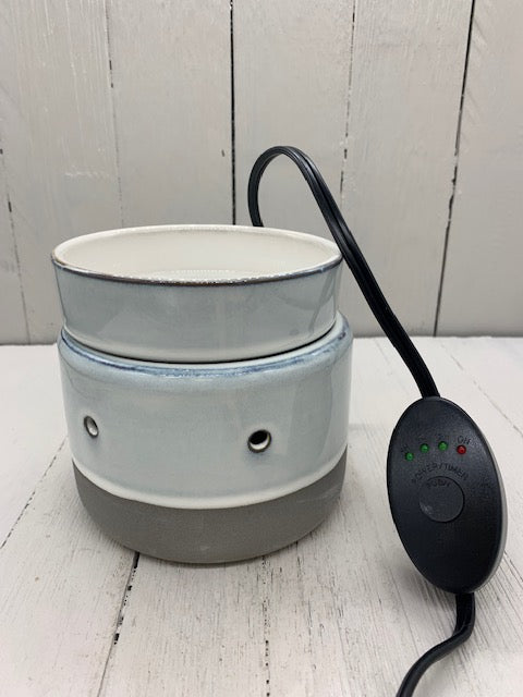 A circular ceramic wax warmer. It is light gray with a band of dark gray on the bottom. There are two holes where light can shine through. A wire is shown with a button on it. It has four lights above it, three green and one red.