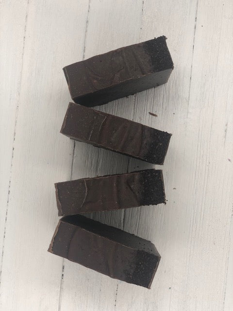 A dark brown soap bar with coffee grounds pressed into the top of the soap.