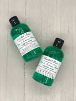 A clear bottle with teal liquid soap inside. A white label reads "Aloe & Summer Herbs".