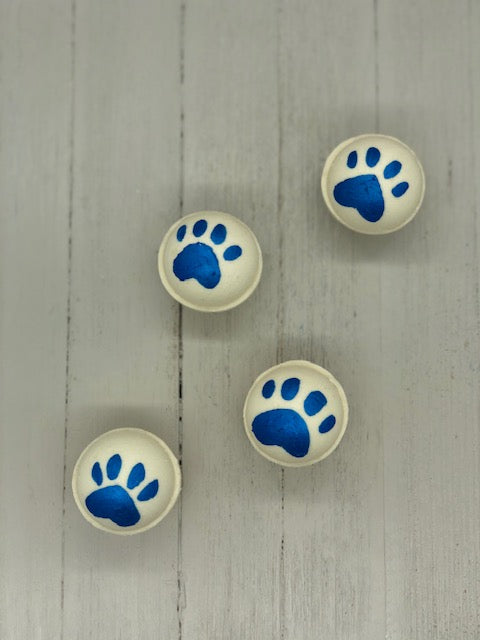 White bath bombs, some painted with blue paw prints, some painted with blue tiger stripes.