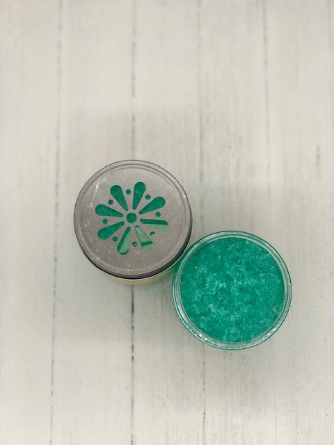 A top down view of two jars. One is full of teal jelly. The other has a tin lid with a daisy cut out on top.